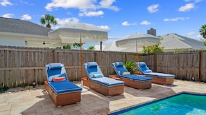 A backyard with a pool, four lounge chairs, and umbrellas.