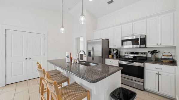 A modern kitchen with white cabinets, granite countertops, stainless steel appliances, and a central island with seating.