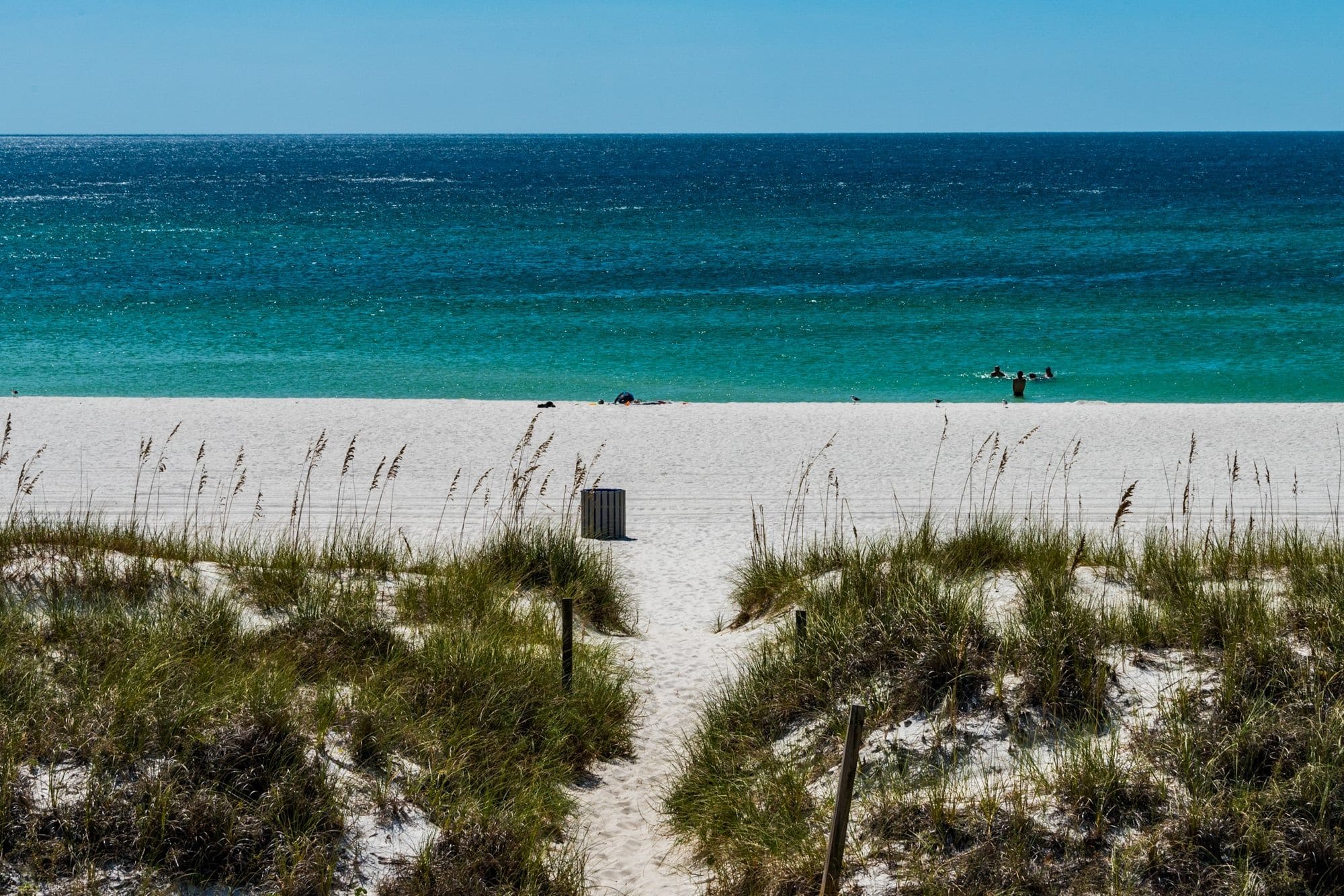 A beach with a clear path leading to the water, surrounded by sand and grass.