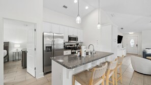 A modern kitchen with white cabinetry, stainless steel appliances, a granite countertop, and a dining area with wicker chairs.