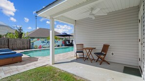 A covered patio with a pool, two wooden chairs, and a table.