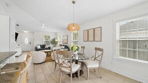 A modern living room with a dining area, white walls, and a ceiling fan.
