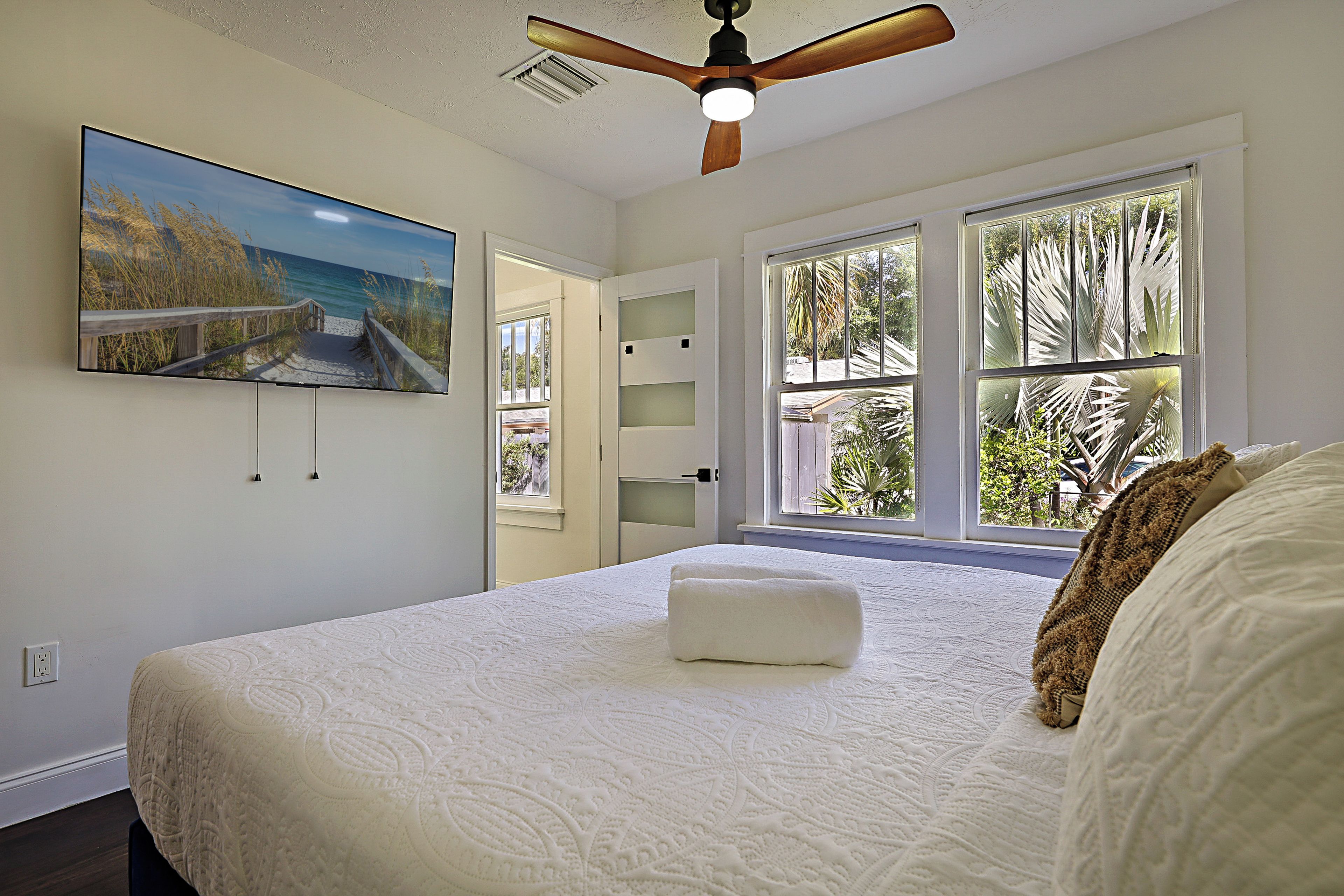 Un dormitorio con una cama grande, ventilador de techo y vistas al exterior a través de las ventanas.