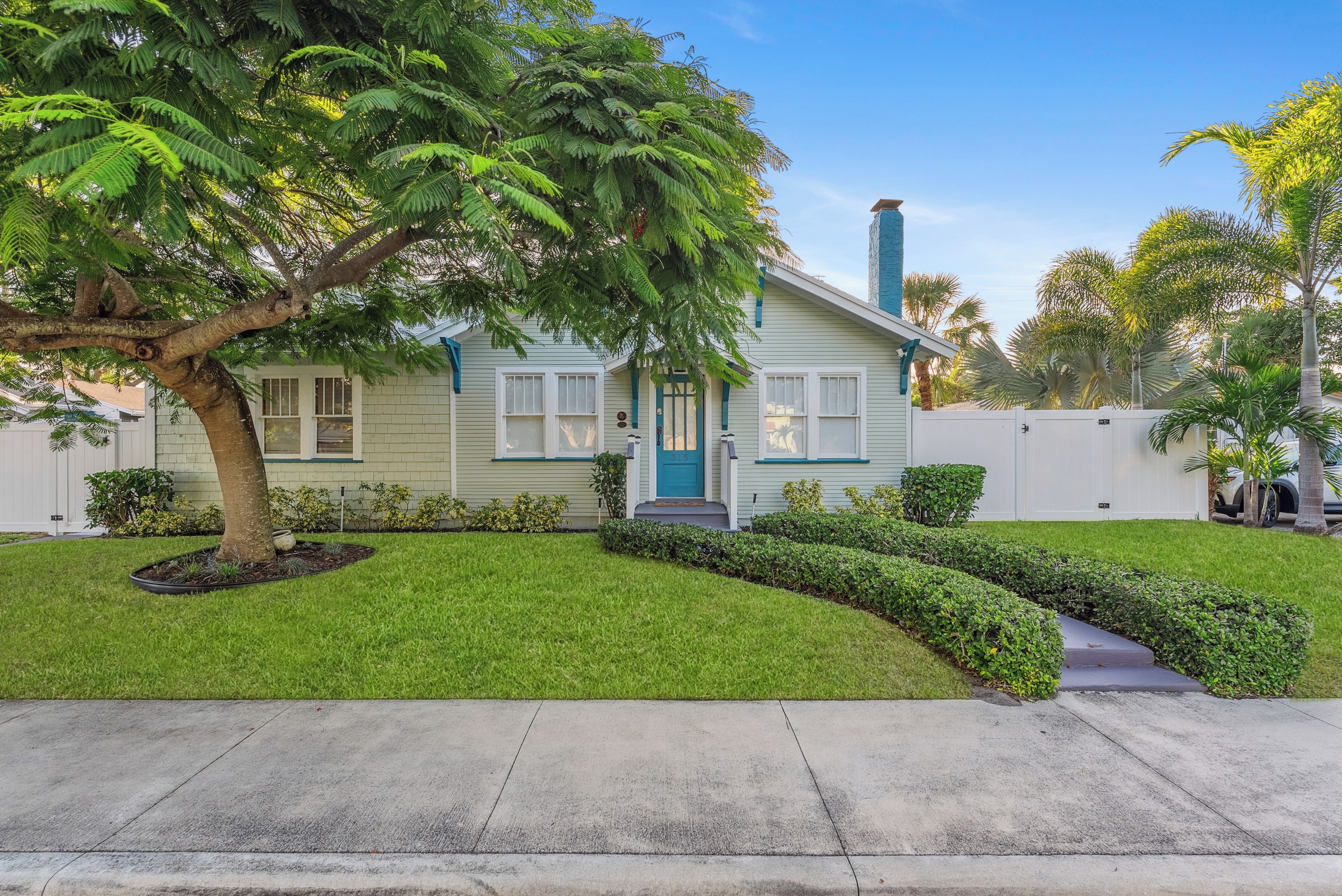 A single-story house with a front yard, a tree, and a white fence.