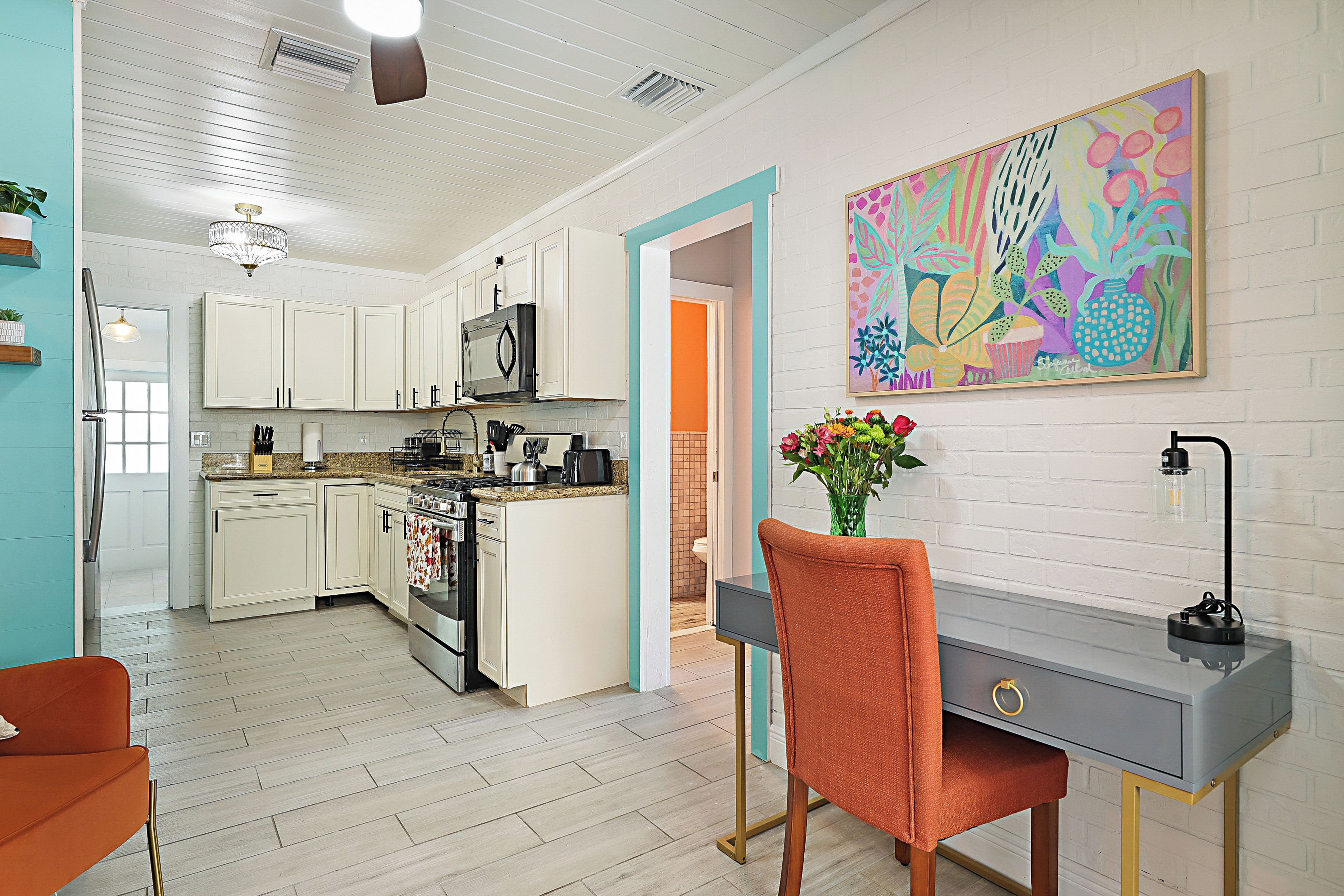 A modern kitchen with white cabinetry, a central island, and a dining area with a gray table and orange chair.