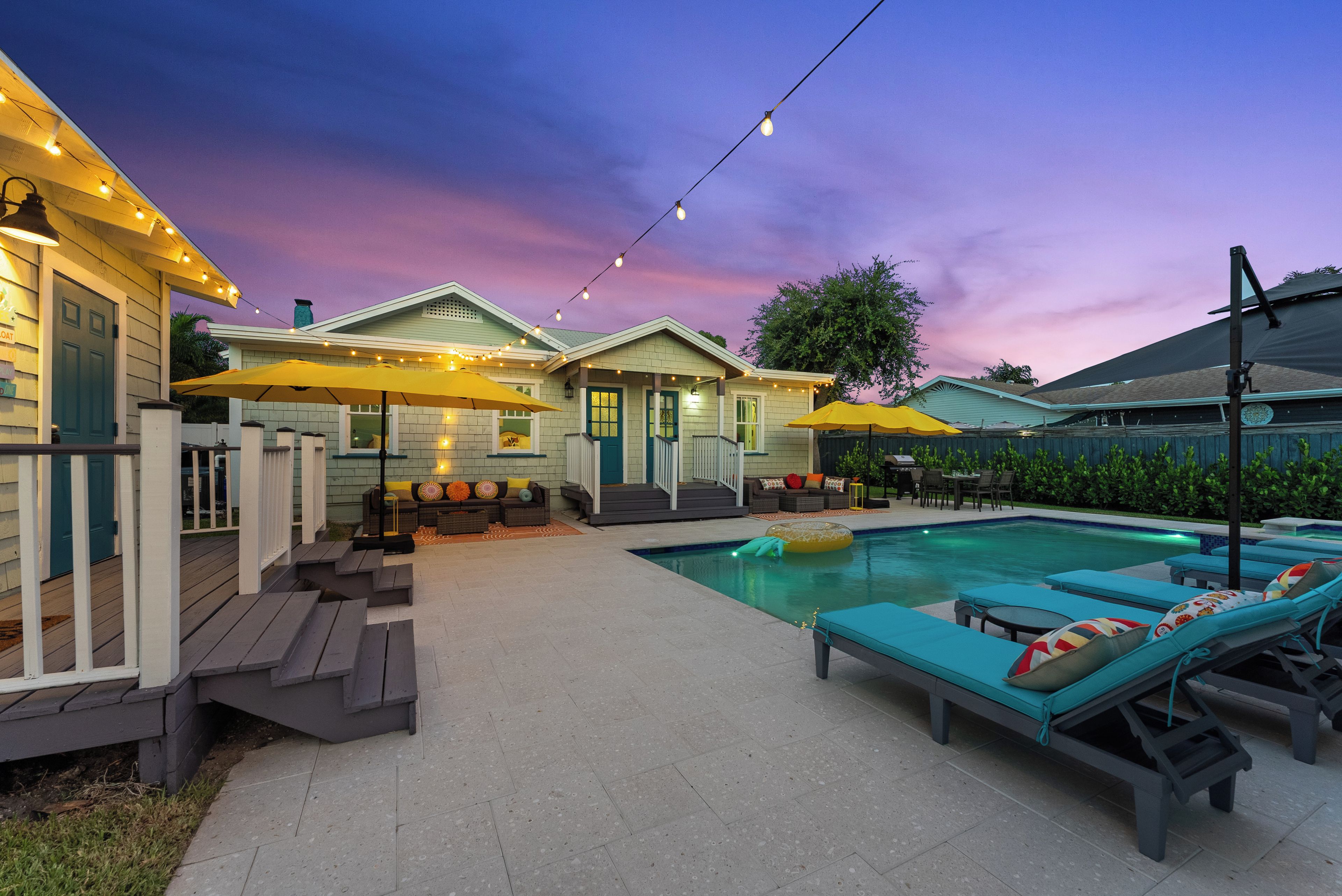 A backyard with a swimming pool, outdoor seating, and string lights.