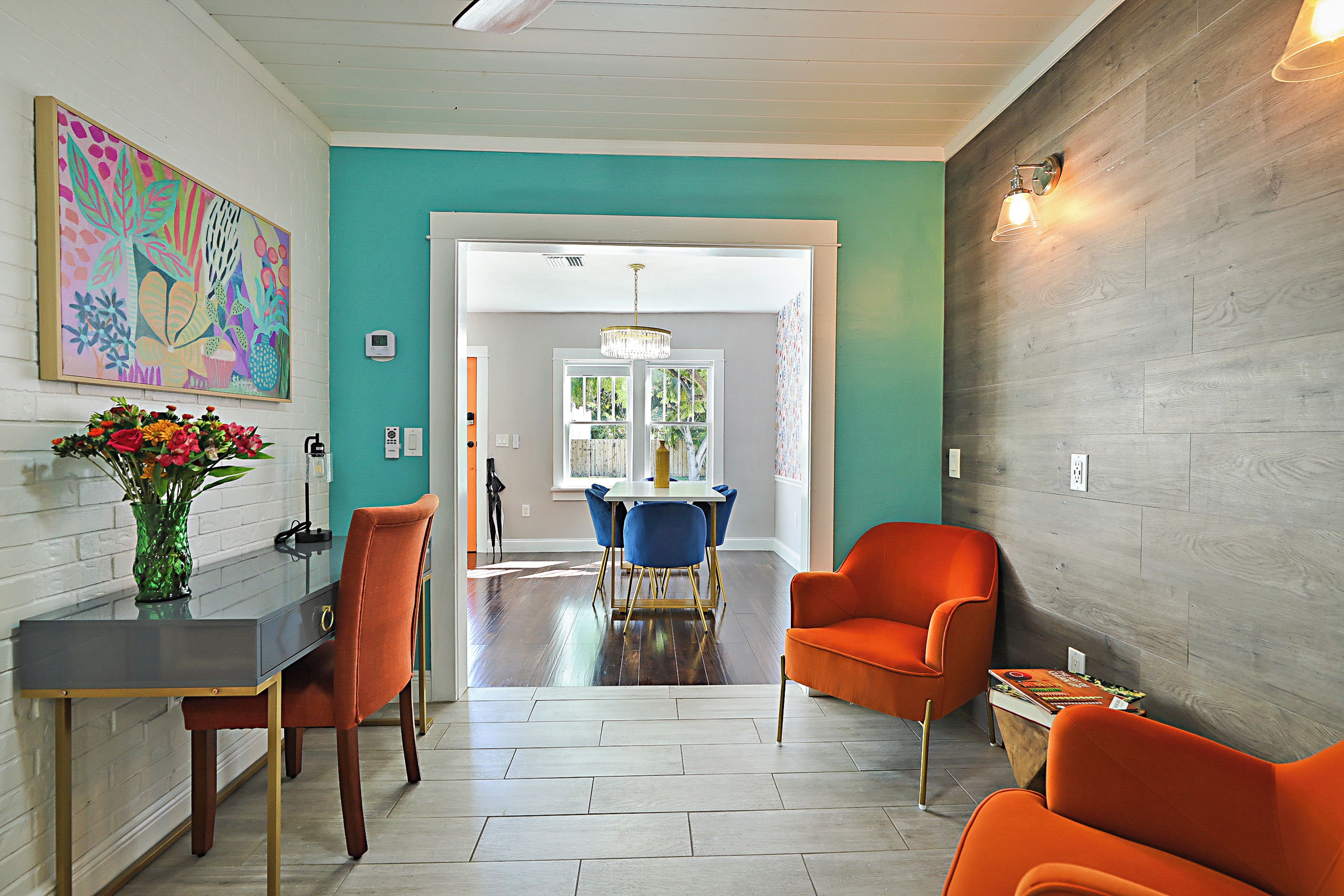 A modern interior with a teal accent wall, a dining area with blue chairs, and a vibrant painting.