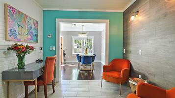 A modern interior with a teal accent wall, a dining area with blue chairs, and a vibrant painting.