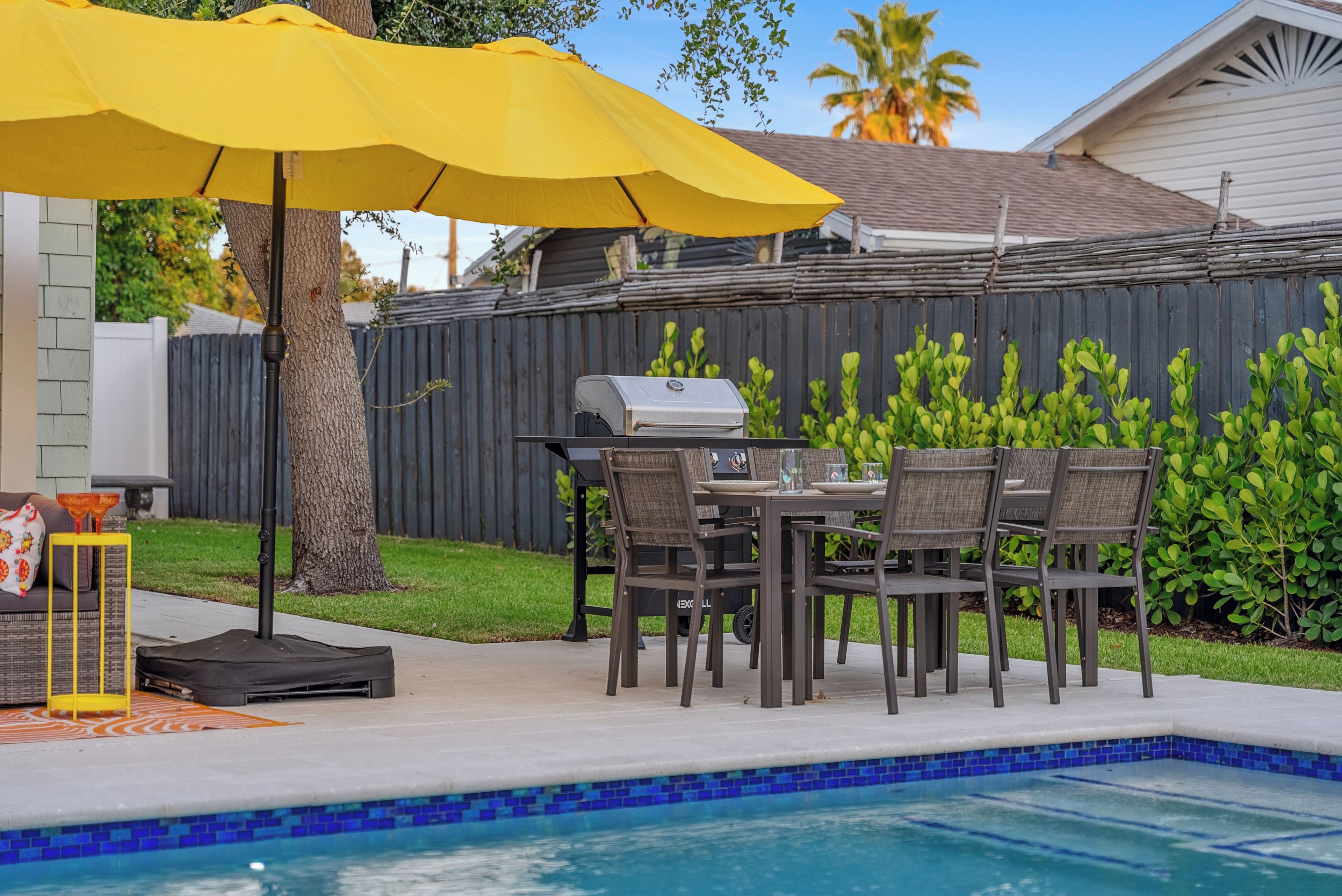 An outdoor patio with a pool, a grill, and a dining area with chairs and a table.