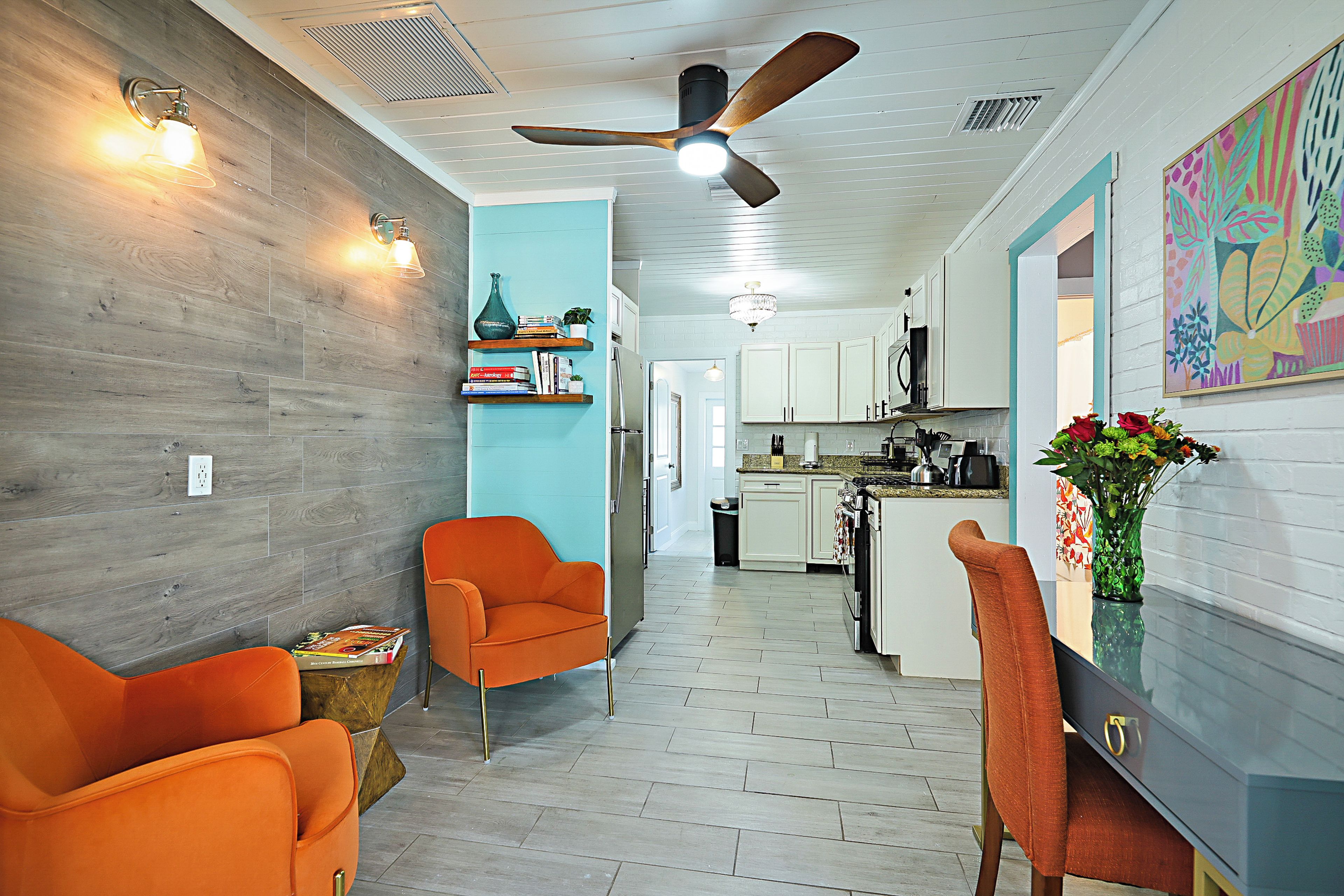 A modern kitchen with white cabinets, a dining area with orange chairs, and a hallway leading to a living room.