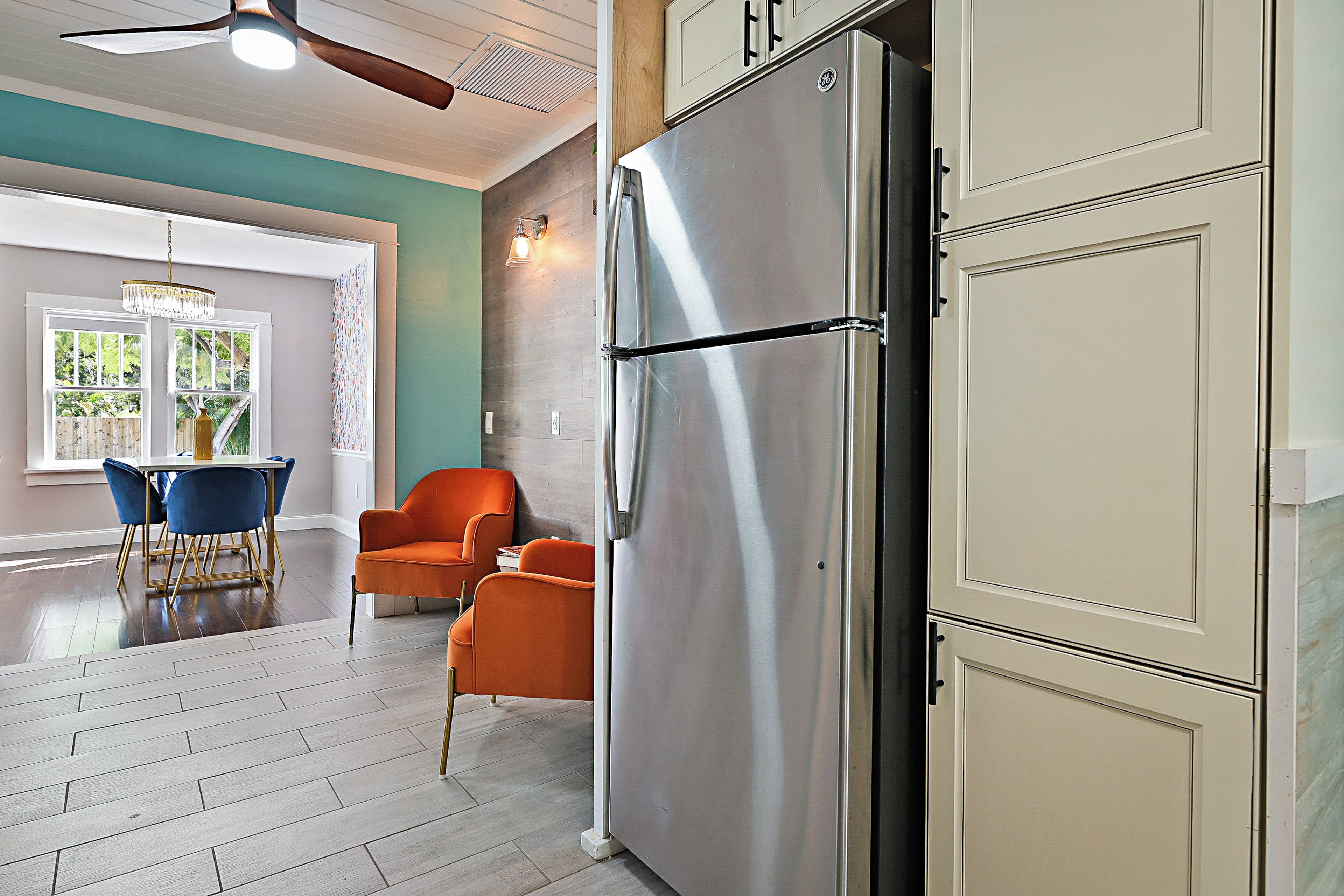 A kitchen with a stainless steel refrigerator, wooden cabinets, and a dining area with blue chairs.