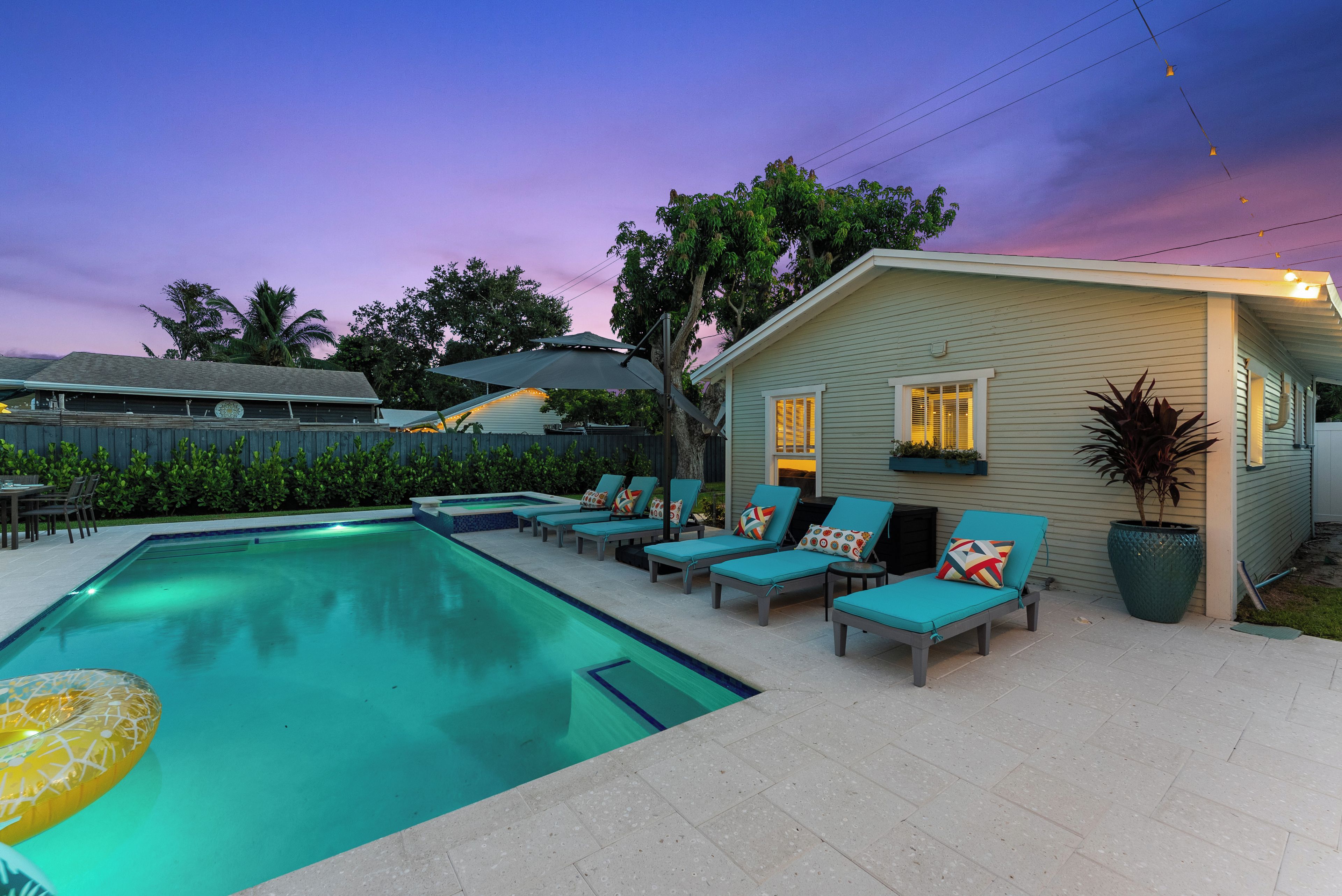 A swimming pool with lounge chairs and a small house with lights.