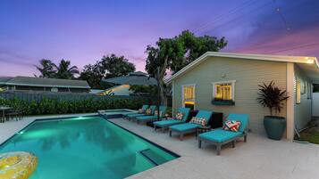 A swimming pool with lounge chairs and a small house with lights.