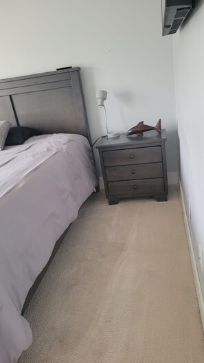 Ein Schlafzimmer mit einem Bett, einem Nachttisch mit Schubladen, einer Lampe und einer Wand-Klimaanlage.