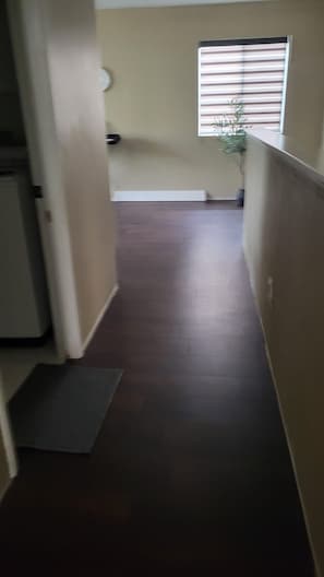 A hallway with a dark wooden floor, a white door on the left, and a window with blinds on the right. - Spacious 4-bedroom home in pleasant Moreno Valley ,nearby golf and lake nearby (Moreno Valley)