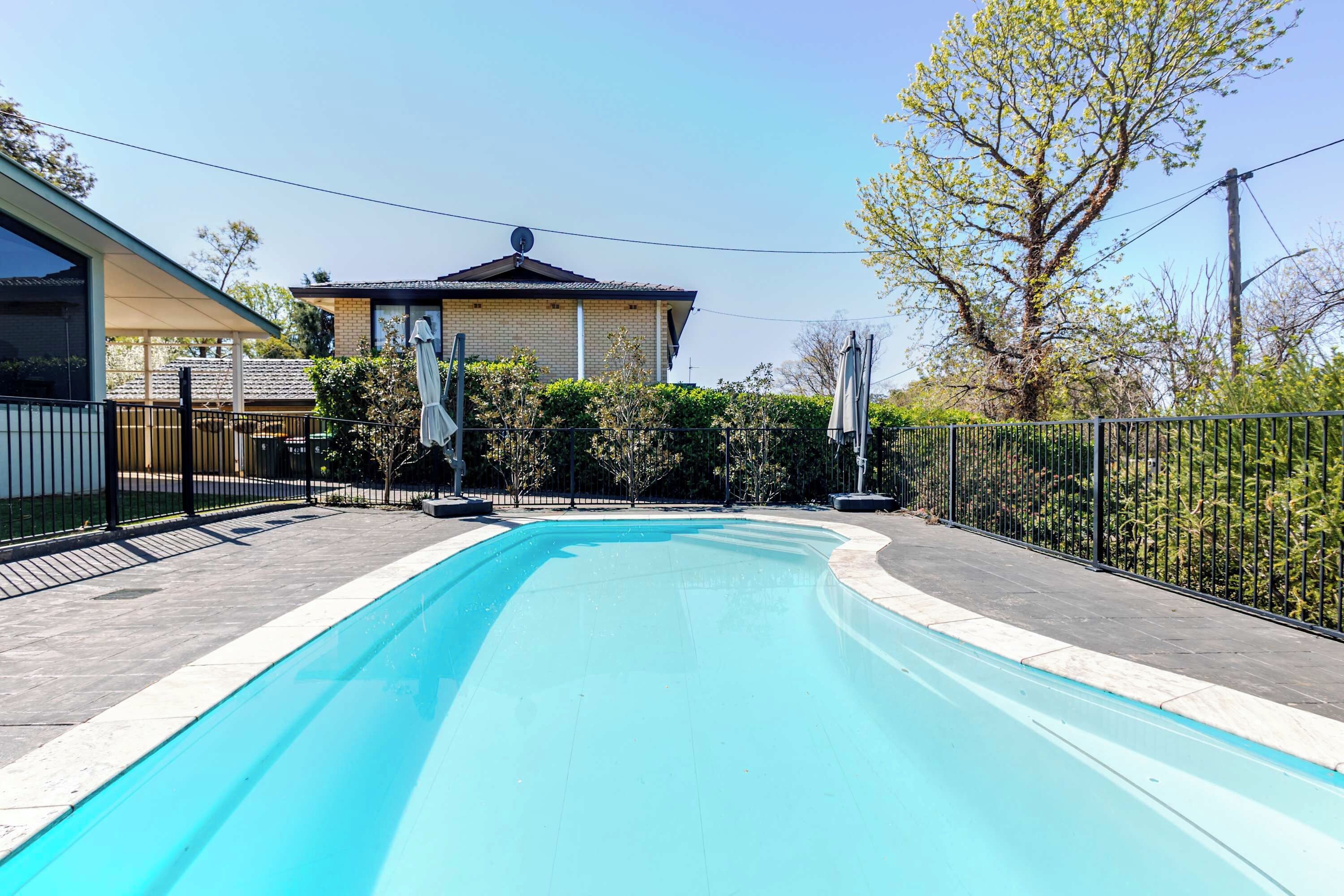 Una piscina amb vora de rajola, envoltada per una tanca metàl·lica, i un edifici amb parabre d'antena al fons.