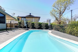 A swimming pool with a tiled edge, surrounded by a metal fence, and a building with a satellite dish in the background. - Summer Daze, Pool & Pet Friendly, Dubbo (Dubbo)