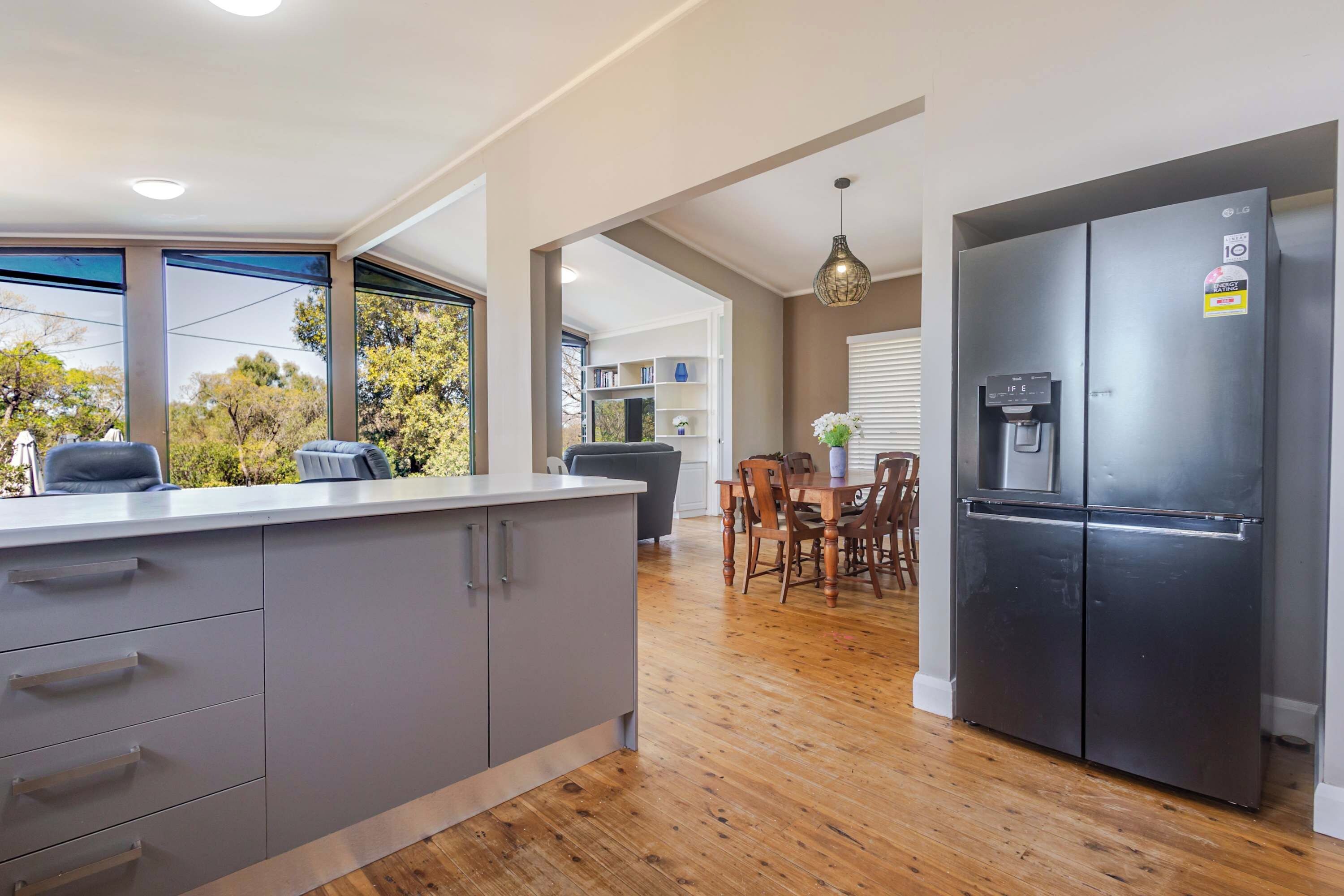 A modern kitchen with a built-in refrigerator, wooden dining table, and a view of the outdoors through large windows.