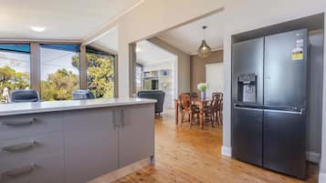 A modern kitchen with a built-in refrigerator, wooden dining table, and a view of the outdoors through large windows.