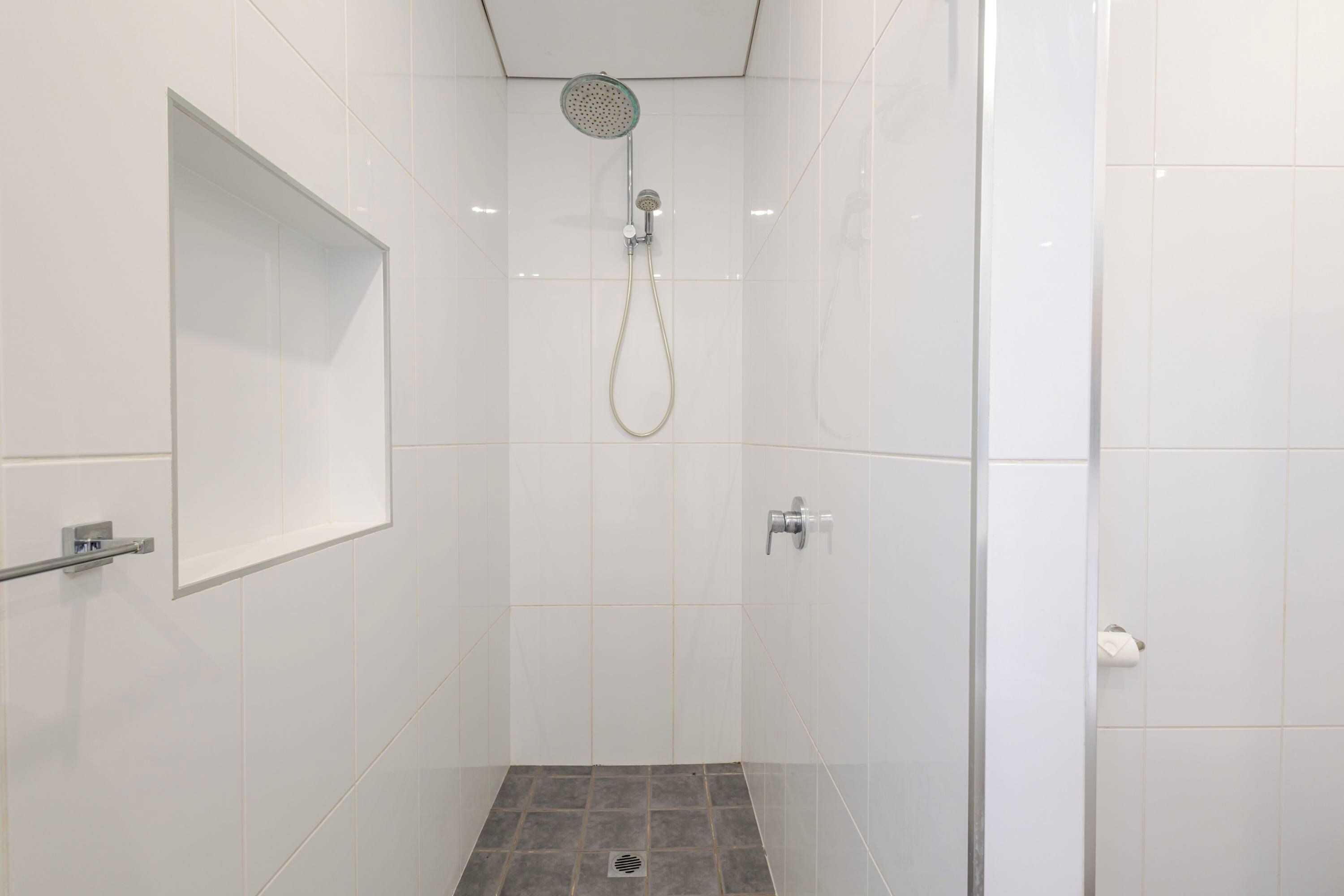 A modern shower with a glass enclosure, a visible drain, and a wall-mounted control panel.
