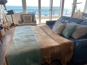 A room with a bed, a sofa, and a view of the ocean.