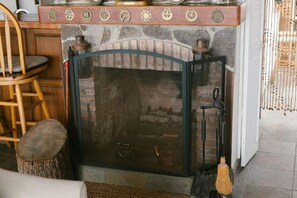 A stone fireplace with a glass door, a wooden chair, and a broom leaning against the wall.