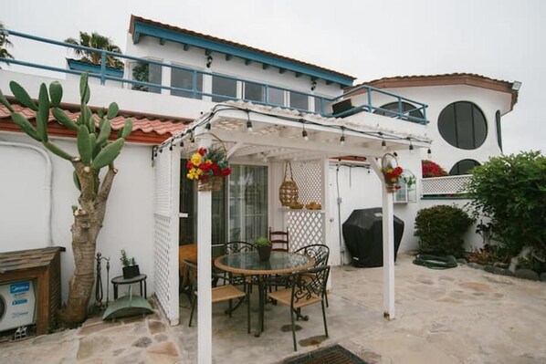 A patio area with a table and chairs, a cactus plant, and a covered seating area with flowers.