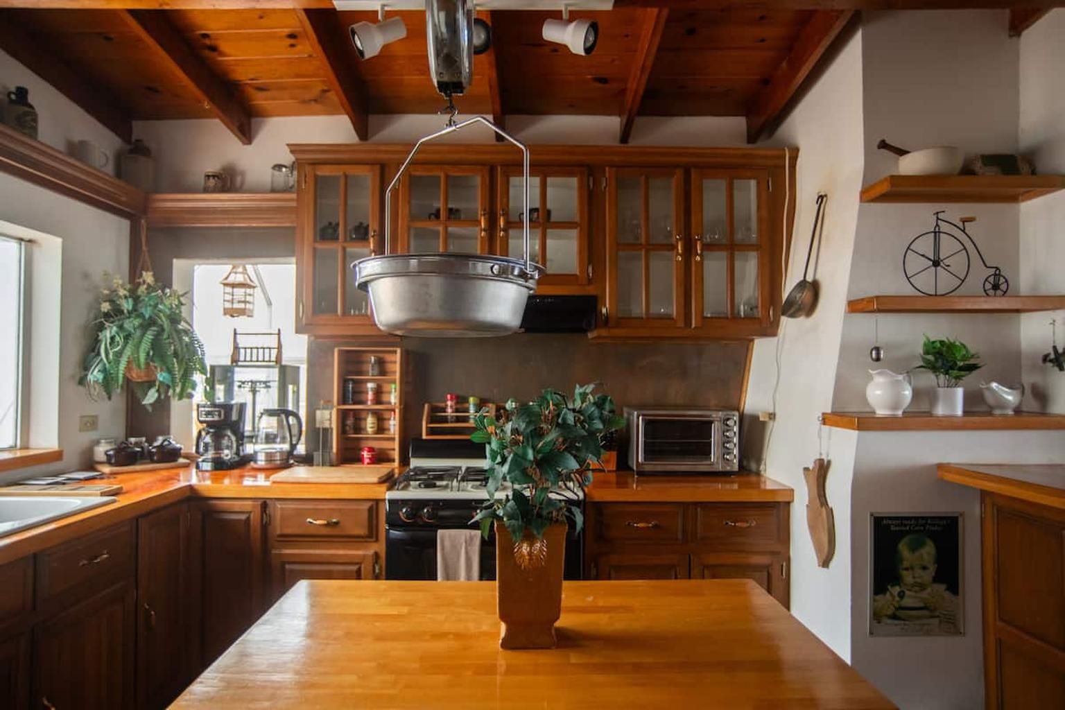 A kitchen with wooden cabinets, a hanging pot rack, a stove, and a coffee maker.