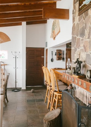 A rustic interior with a stone wall, wooden ceiling beams, and a dining area with wooden chairs and a table.