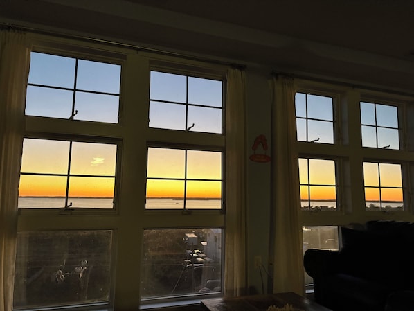 Een kamer met grote ramen met uitzicht op een zonsondergang, een bank en een bord aan de muur.