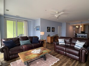 A living room with two leather sofas, a wooden coffee table, and a ceiling fan. -  2-bedroom beach condo steps from the beach with amazing sunsets (Virginia Beach)