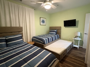 Habitación de hotel con dos camas, ventilador de techo, televisor y mesita de noche con lámpara.