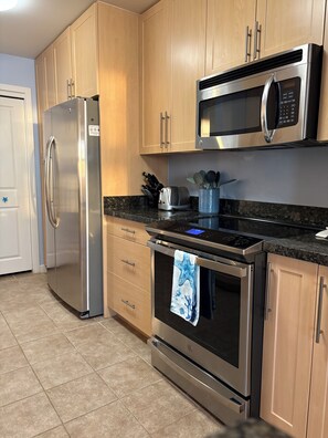 A kitchen with stainless steel appliances, wooden cabinets, and a granite countertop. -  2-bedroom beach condo steps from the beach with amazing sunsets (Virginia Beach)