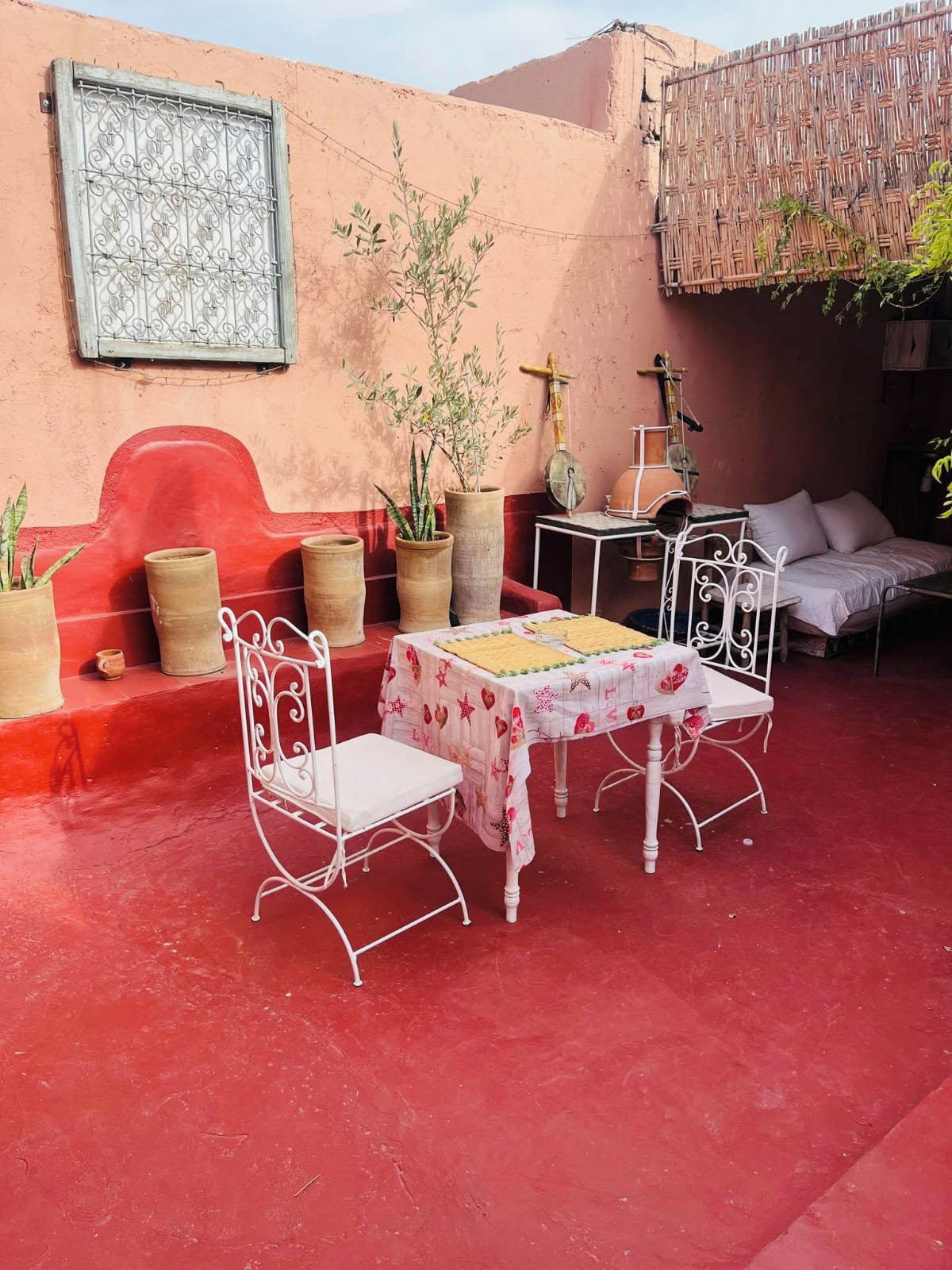 An outdoor seating area with a table and chairs, potted plants, and a red wall.