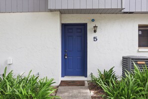 A blue door with a number 5 sign above it, a white wall, and green plants in the foreground. - Attention football fans!  Charming 3-bedroom townhome close to UF. Small pet ok (Gainesville)