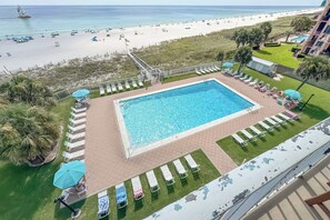 Ein Poolbereich mit Liegestühlen und Sonnenschirmen, im Hintergrund ein Strand und Blick auf den Ozean.