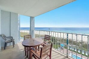 Een balkon met een tafel en stoelen, met uitzicht op een strand en een heldere lucht.