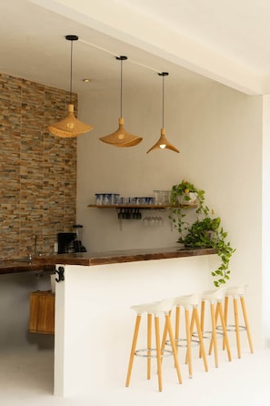 A modern kitchen with a brick backsplash, pendant lights, a bar area with stools, and a plant. - Casa Corazon Zen-Double Suite (Petatlán)