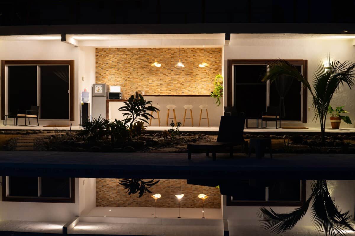 A modern outdoor seating area with a pool, a stone wall, and hanging lights.