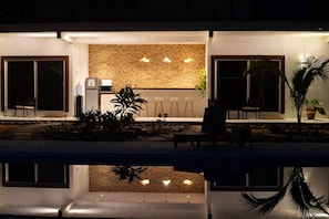 A modern outdoor seating area with a pool, a stone wall, and hanging lights.