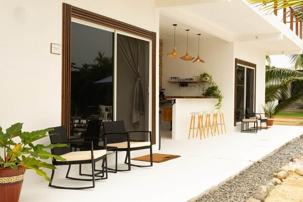 An outdoor seating area with a table and chairs, a bar area with stools, and a potted plant.