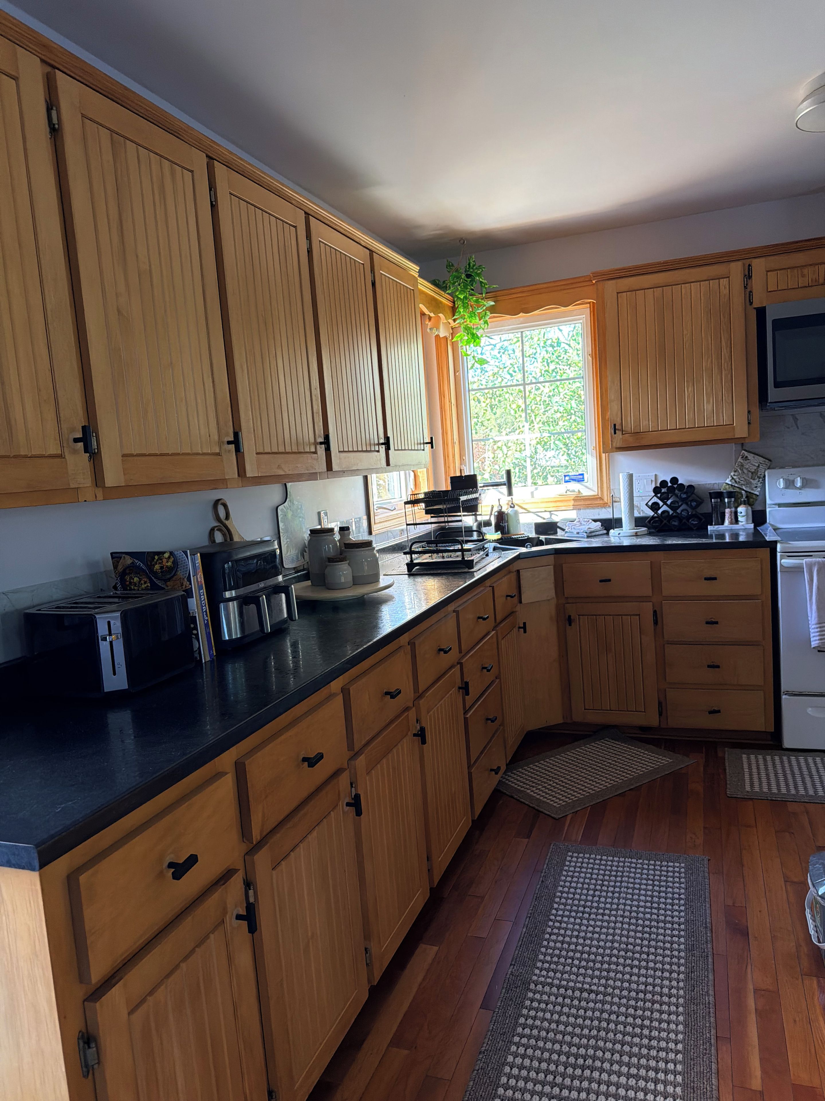 A kitchen with wooden cabinets, a black countertop, a stove, and a window with a view of greenery.