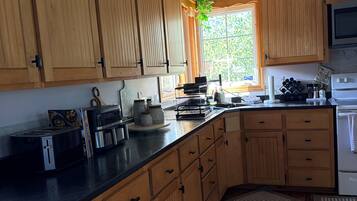 A kitchen with wooden cabinets, a black countertop, a stove, and a window with a view of greenery.