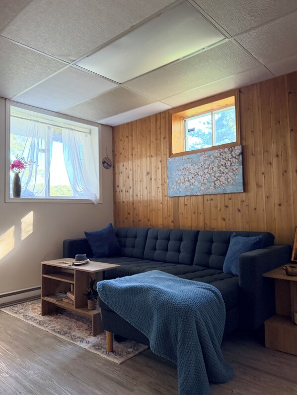 Una sala de estar acogedora con un sofá azul oscuro, una mesita de madera y una ventana con cortinas de gasa.