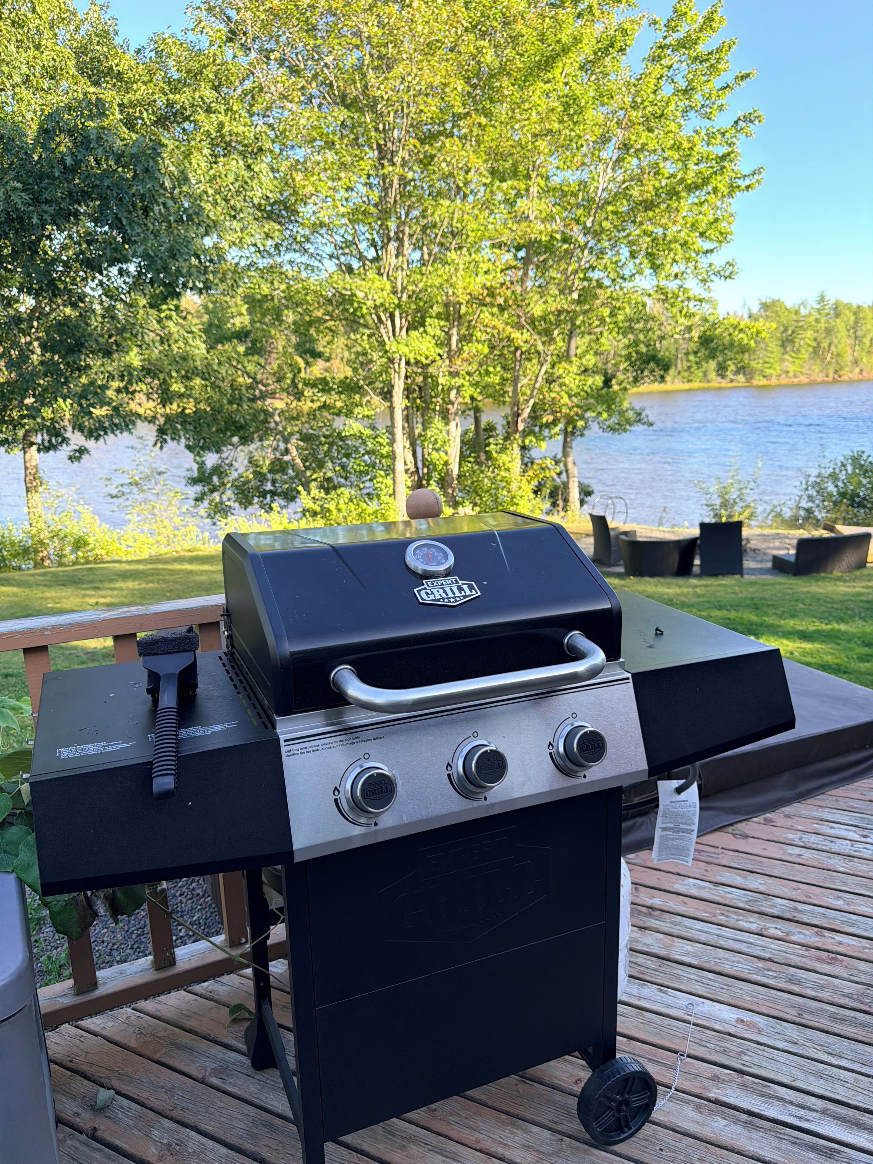 A barbecue grill on a wooden deck with a lake view.