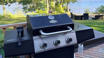 A barbecue grill on a wooden deck with a lake view.
