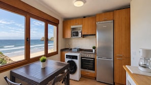 A kitchen with a view of the beach, a washing machine, a stove, and a refrigerator. - House in Llanes | Directly on the beach | Rebellín (Celorio (Llanes))