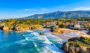 A coastal town with a beach, rocky coastline, and mountainous background. - House in Llanes | Directly on the beach | Rebellín (Celorio (Llanes))