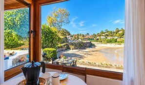 A room with a view of a beach and houses. There is a table with a kettle, cups, and a plate. - House in Llanes | Directly on the beach | Rebellín (Celorio (Llanes))