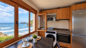 A kitchen with a view of the ocean, wooden cabinets, a stainless steel refrigerator, and a washing machine. - House in Llanes | Directly on the beach | Rebellín (Celorio (Llanes))